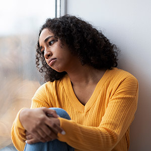 Sad woman looking out window; seasonal depression and SSD disability claims help. 